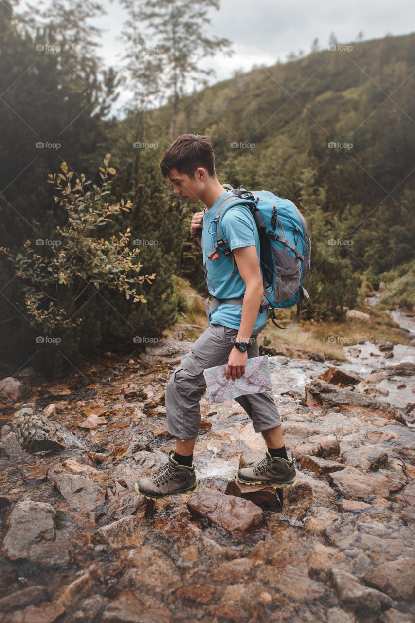 Teenage boy hiking on rock near forest