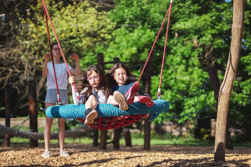 Two beautiful caucasian brunette girls with emotions of fear on their faces ride on a round hanging swing in a public park on a playground on a clear sunny day, close-up side view.