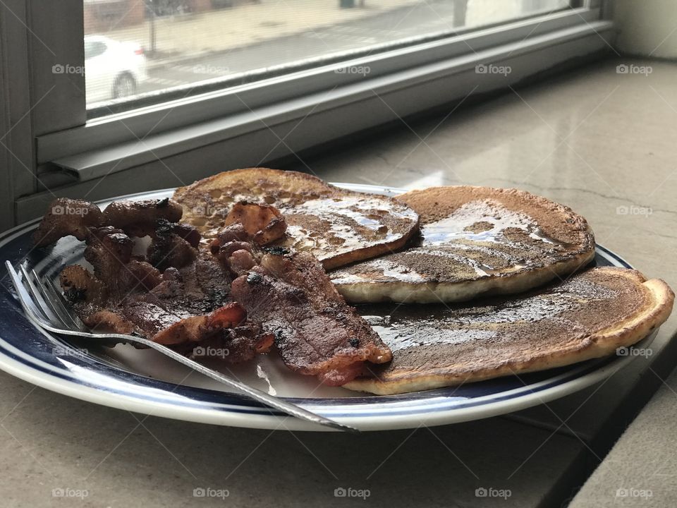 Breakfast of pancakes and bacon on plate with fork in windowsill