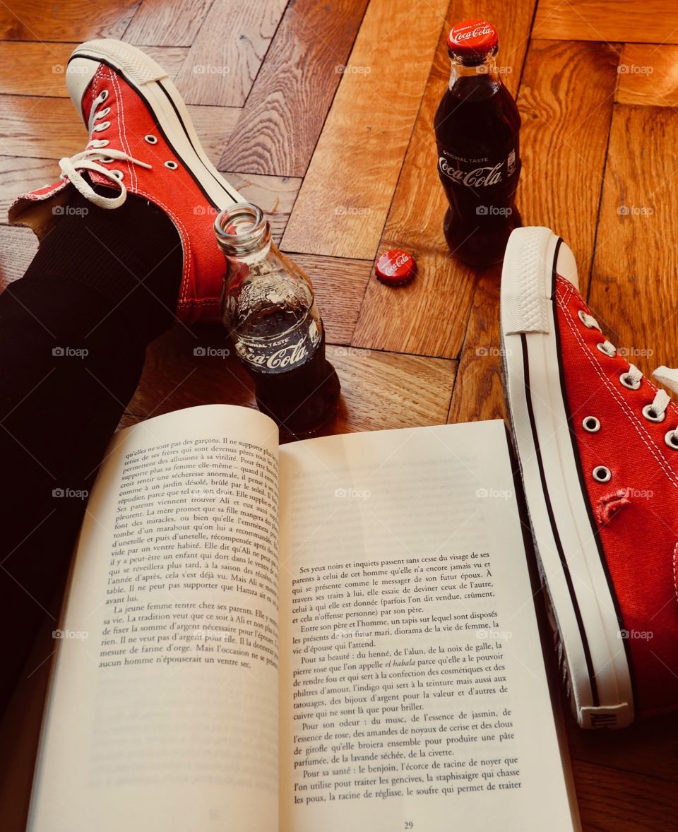 Coca Cola bottles on hardwood floor with red sneakers and a book.