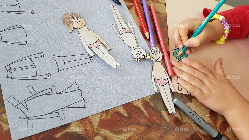 Child is drawing clothing to dress paper people