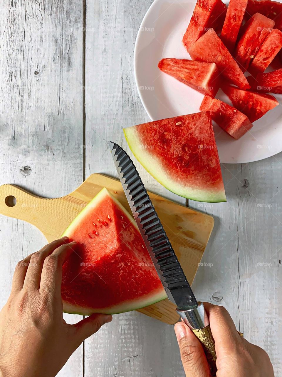 Cutting a red and fresh watermelon on a wooden surface.