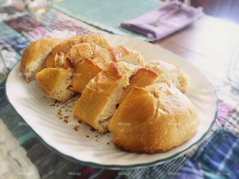 Fresh out of the oven homemade golden crusty baked bread sliced and on the table on a plate