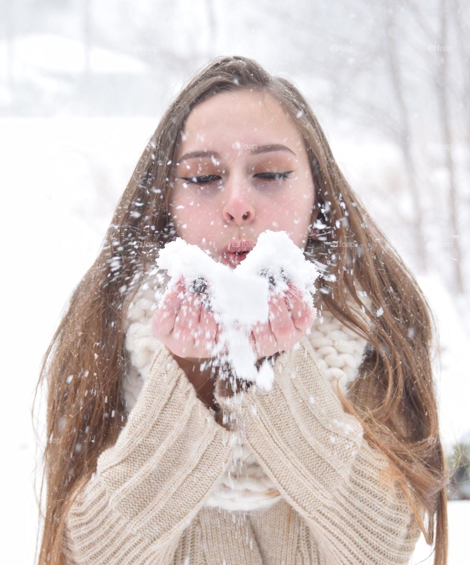 Final snowstorm of winter season, pretty young woman blowing snowflakes into the air