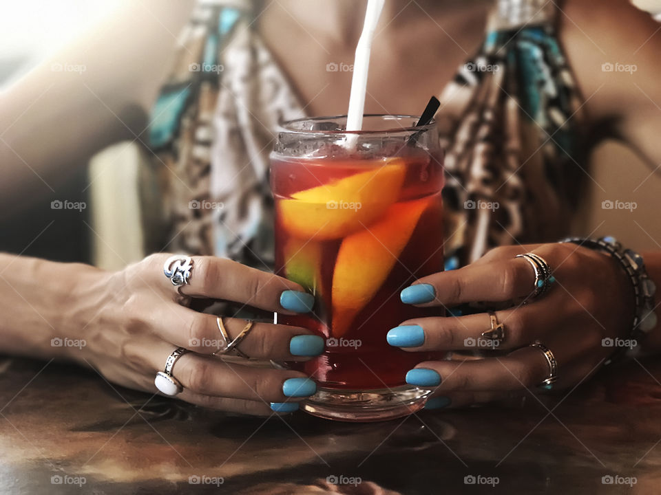 Summer tropical cocktail holding by woman blue manicured hands with fashionable jewelry accessories 