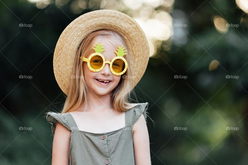 Candid lifestyle portrait of happy little Caucasian girl with sunglasses and straw hat 