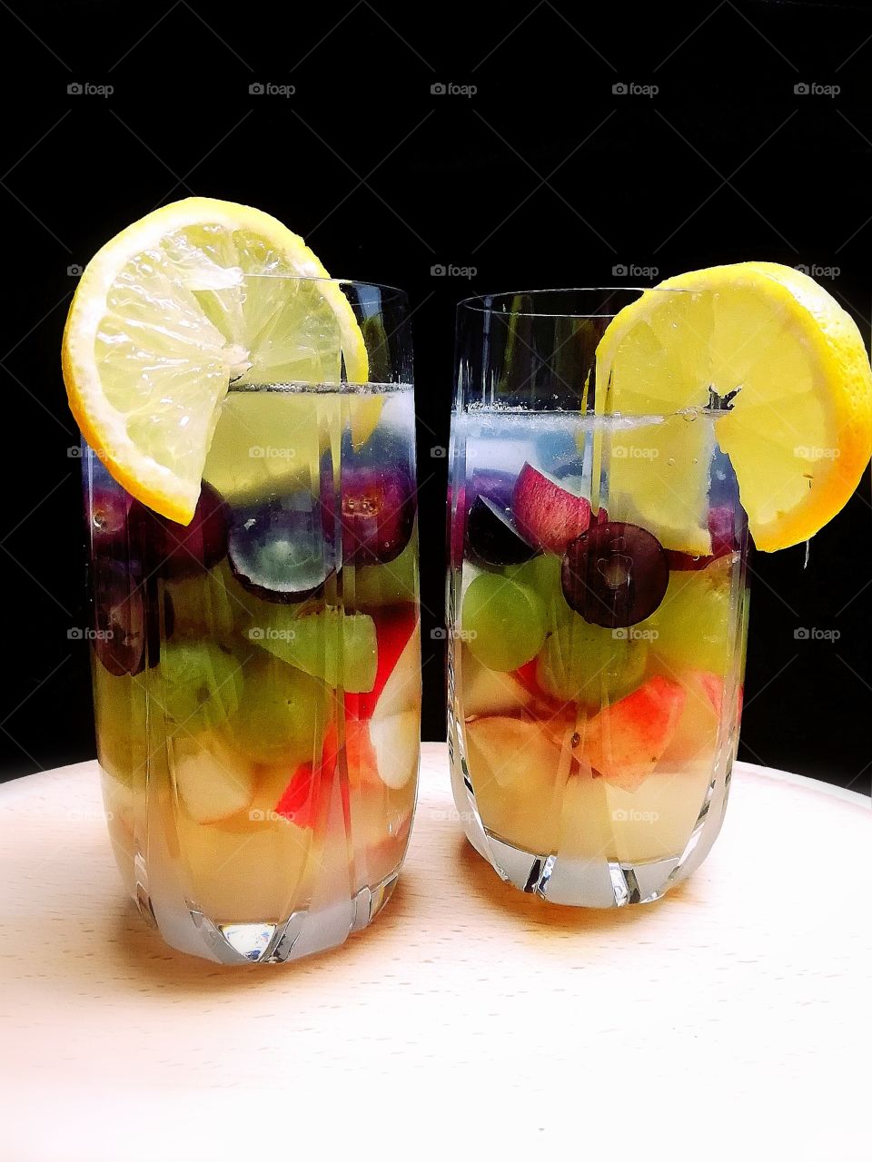 Non-alcoholic refreshment in tropical day with lemon, lime, grapes, apples and ice in one glass.