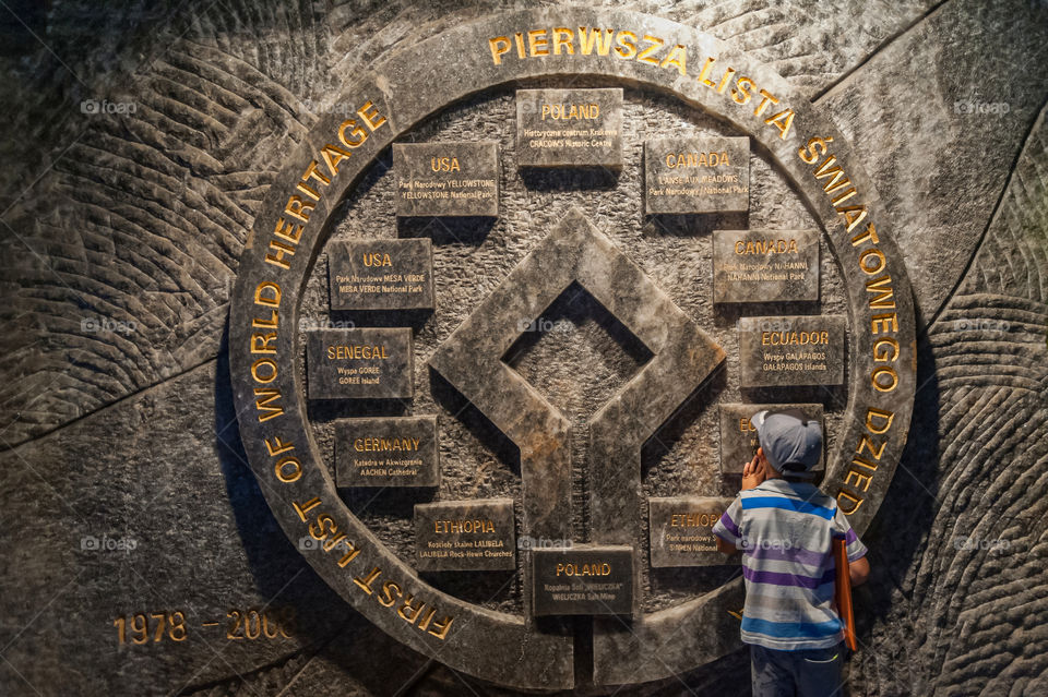 Little boy standing in front of a big information sculpture carved from solid salt rock wall in underground tunnel in Wieliczka Salt Mine in Poland. This is the oldest and still producing salt mine in the world.