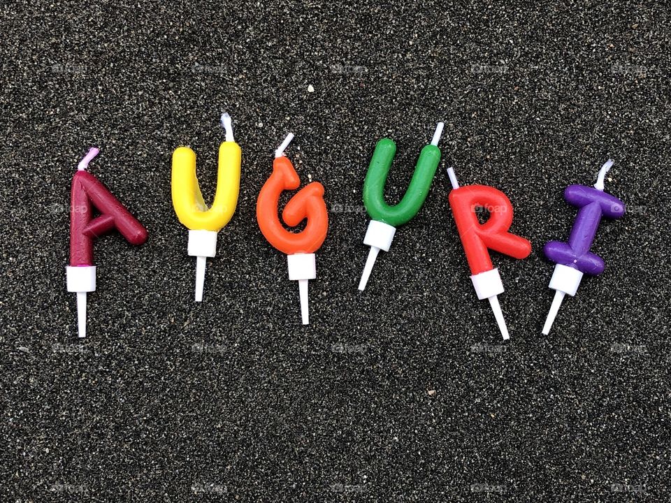 Auguri, Italian Happy Birthday multicolored cake candles over black volcanic sand 