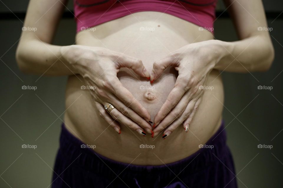 Faceless pregnant woman holding heart shaped hands on her belly 