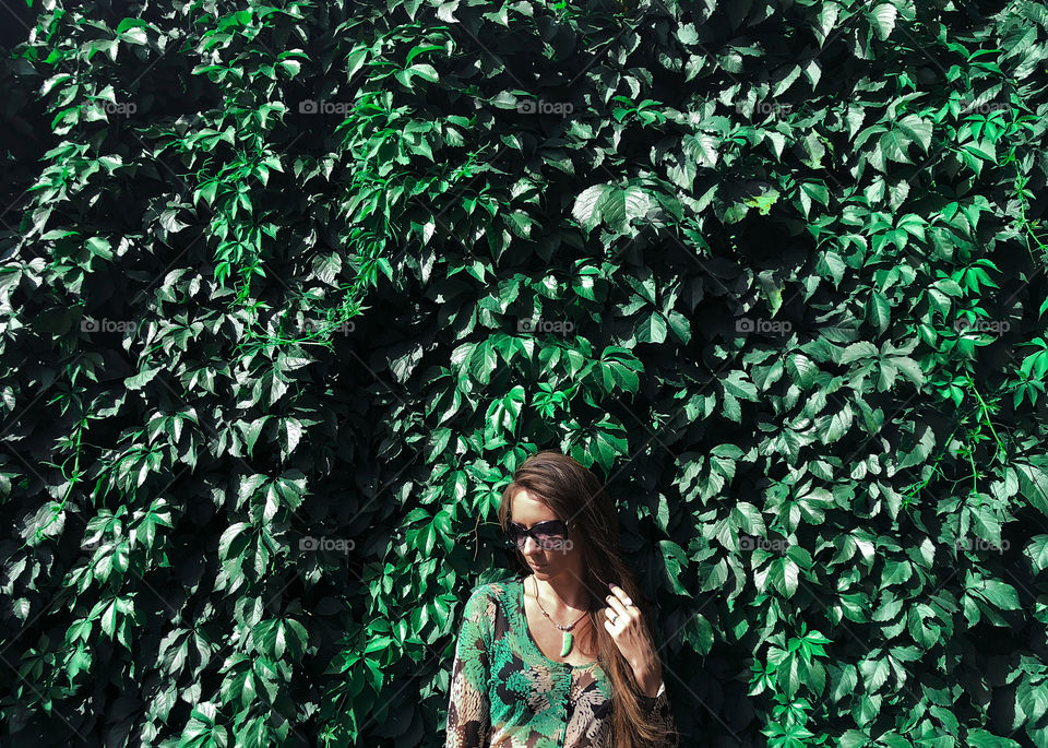 Young woman in green clothes in front of green leaves 