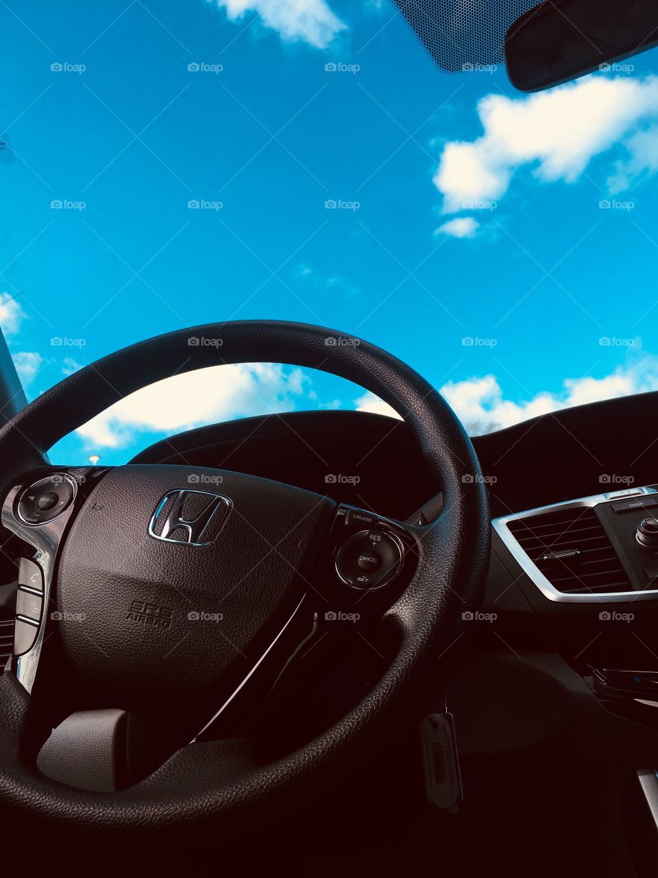 A photo looking up at a sleek, black Honda steering wheel with a bright blue sky behind it 