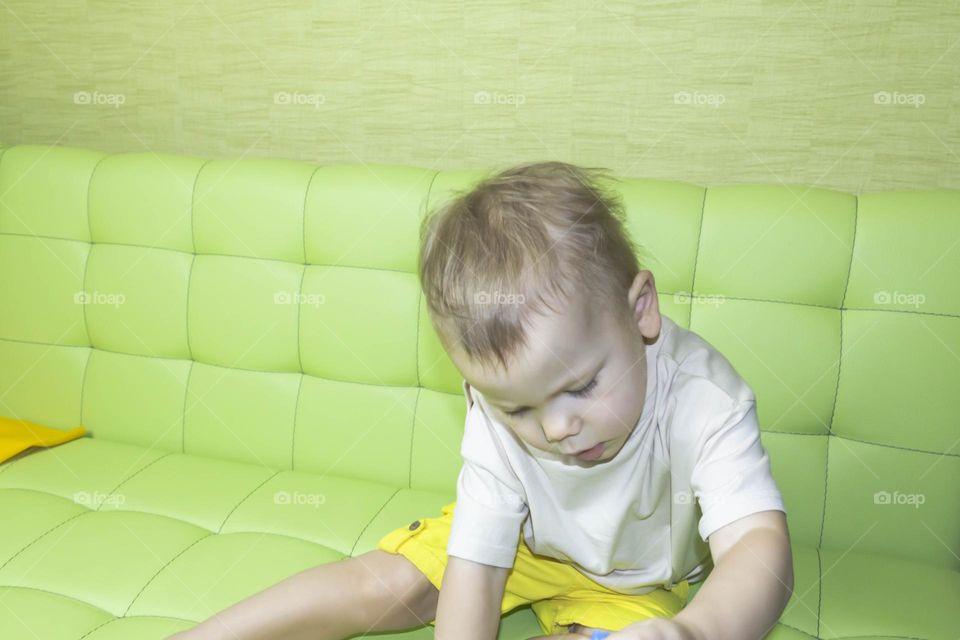 The child is having fun playing a bright pyramid educational toy, sitting on a green sofa.