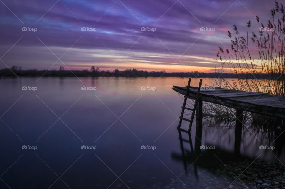 long exposure photo of the small wooden deck on a lake, purple sunset and beautiful clouds