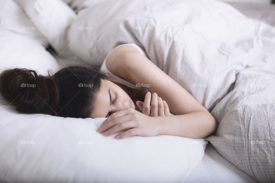 A lady sleeping under a white blanket 