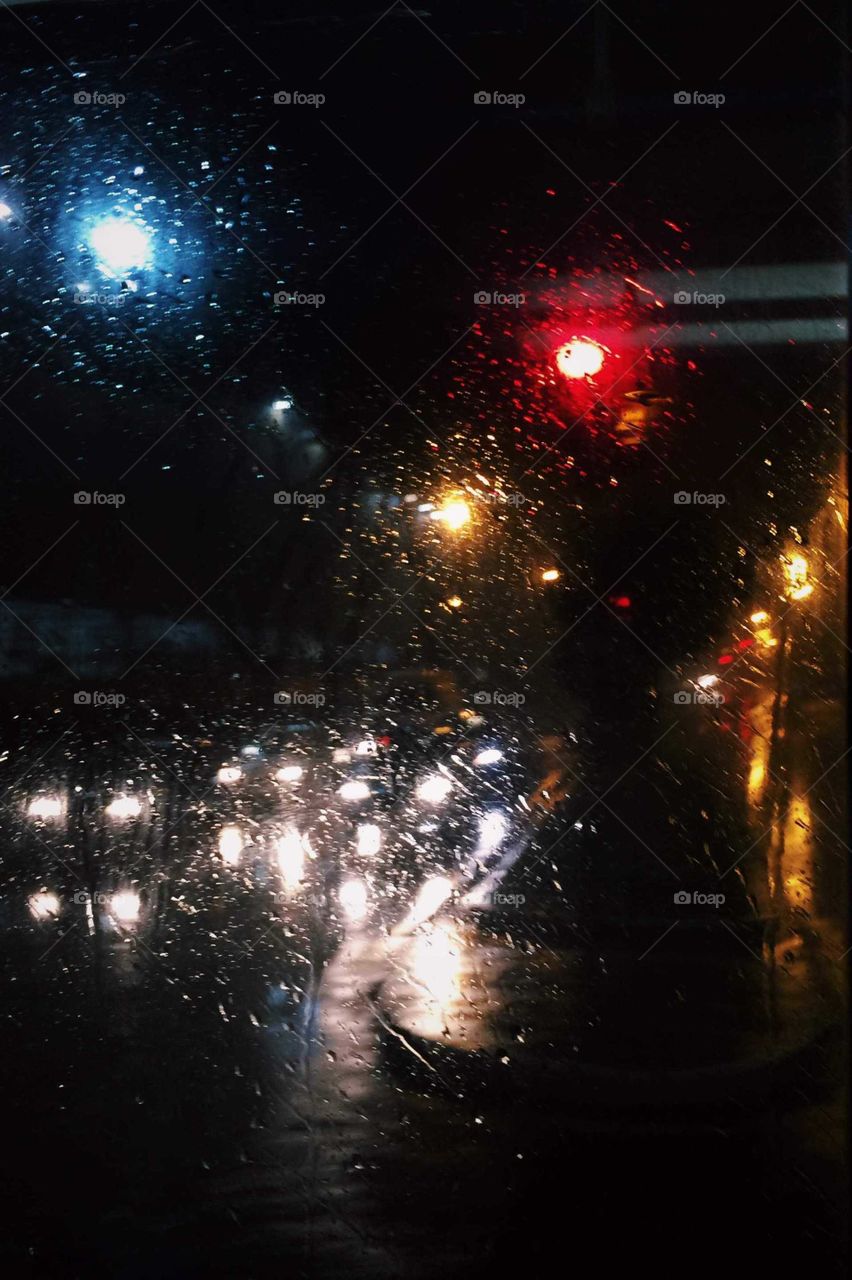 Beautiful shot of a rainy window, showing the traffic lights, and de wet window. Moody shot of the rain in the city.