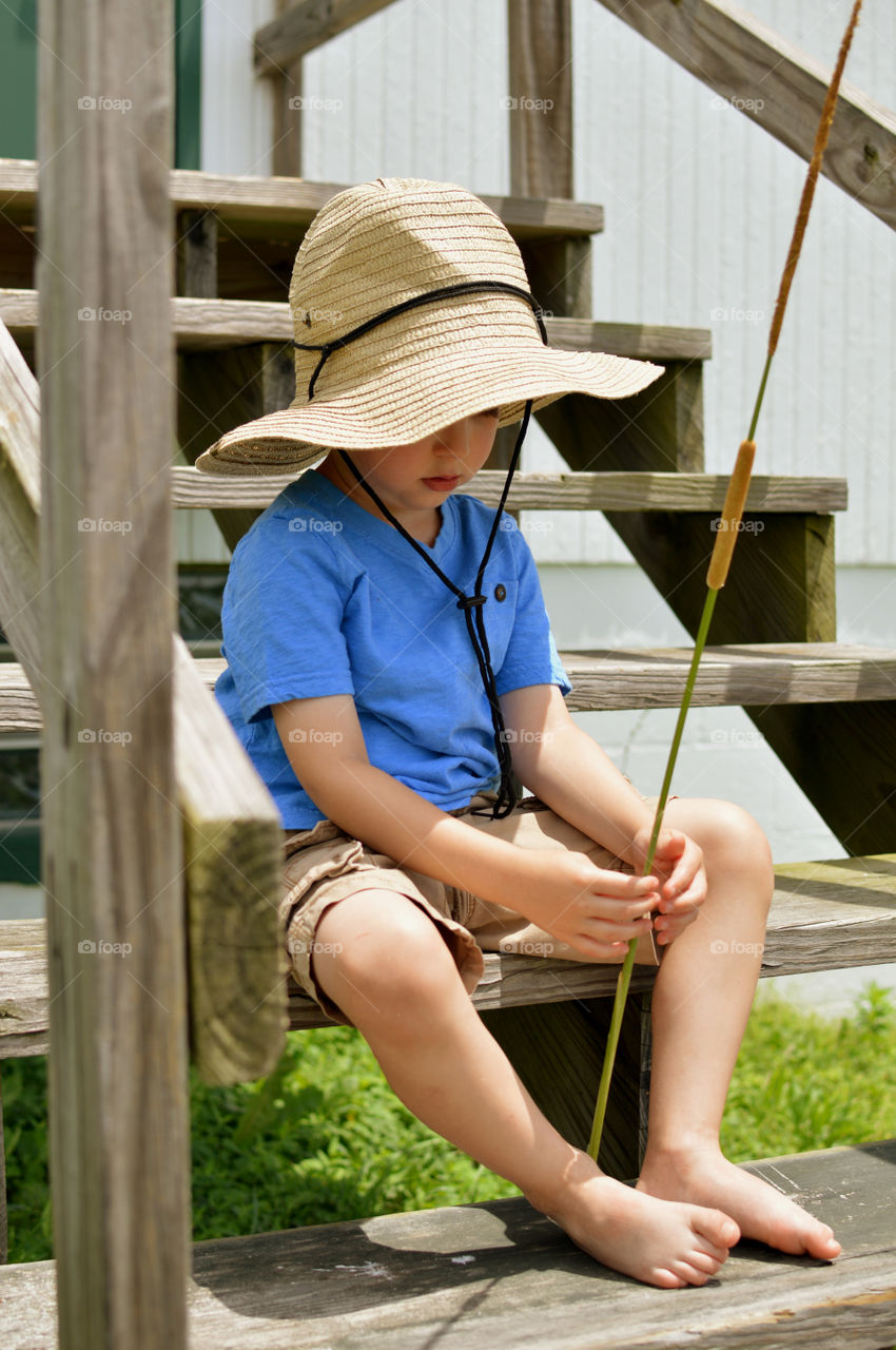 Young boy wearing a cowboy hat and sitting barefoot on wooden stairs outdoors