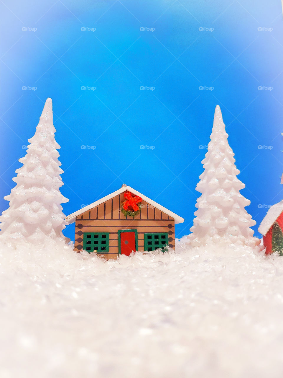 Winter miniature scene of a log cabin and two snow covered pine trees surrounded by snow.