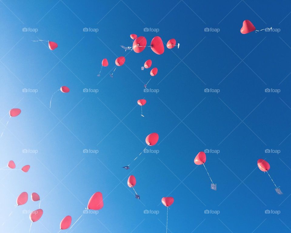 Heart-shaped helium balloons flying into the blue sky with a message attached to them.