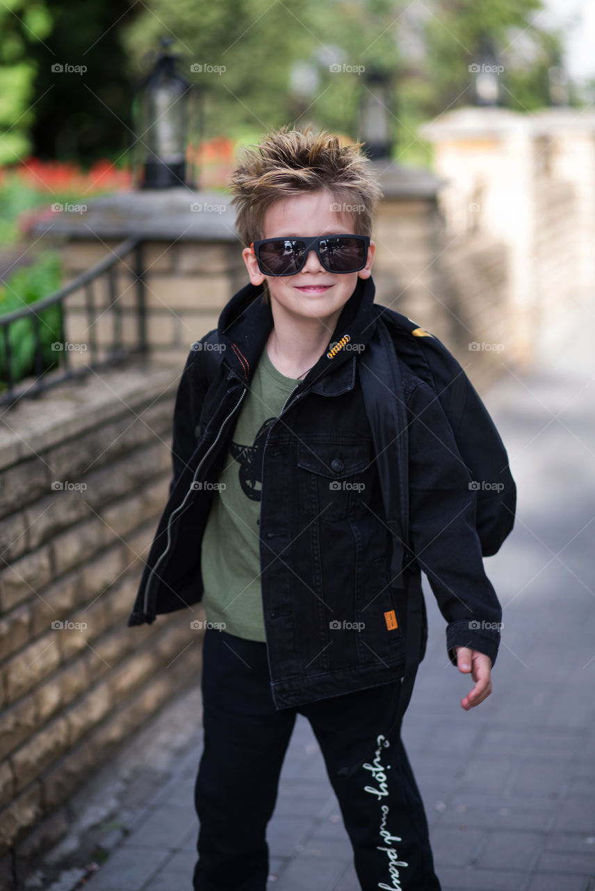 stylish boy in black clothes and glasses is walking along the street.  baby five years old, beautiful blond