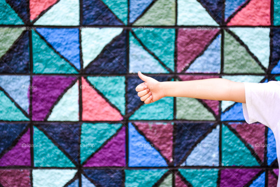 Person's hand giving a thumbs up in front of a colorful geometric patterned urban wall