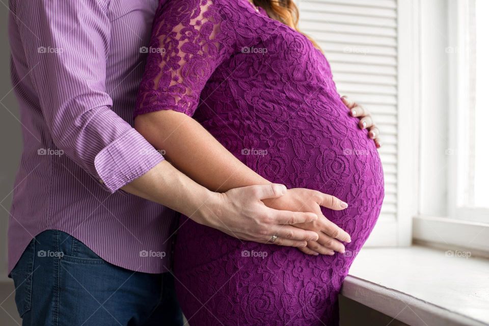 Pregnant woman with her husband hugging a belly 