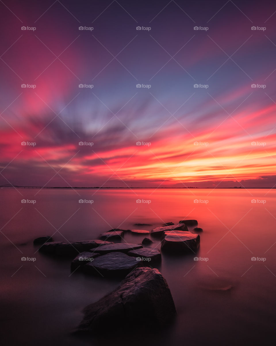 A beautiful vibrant sunset fills the sky with pink and orange colors, as the gorgeous light is reflected on the rocks and body of water in the foreground. 