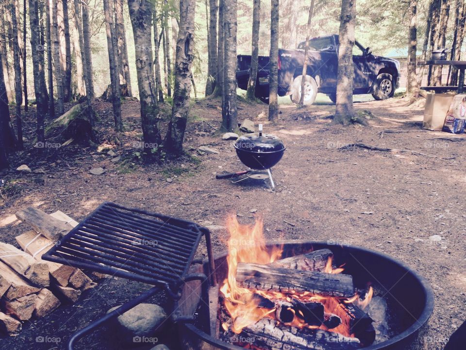 Campfire, camping grill, truck in the background, portable grill - the great outdoors. 