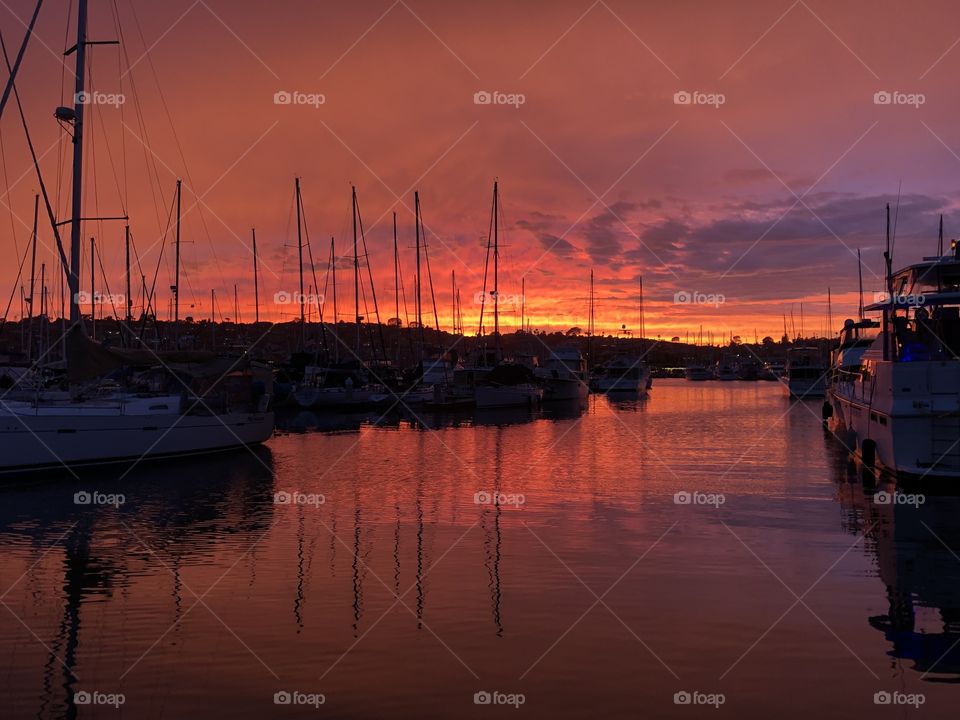 Blazing red orange sunset in a marina with reflections of masts on calm water 