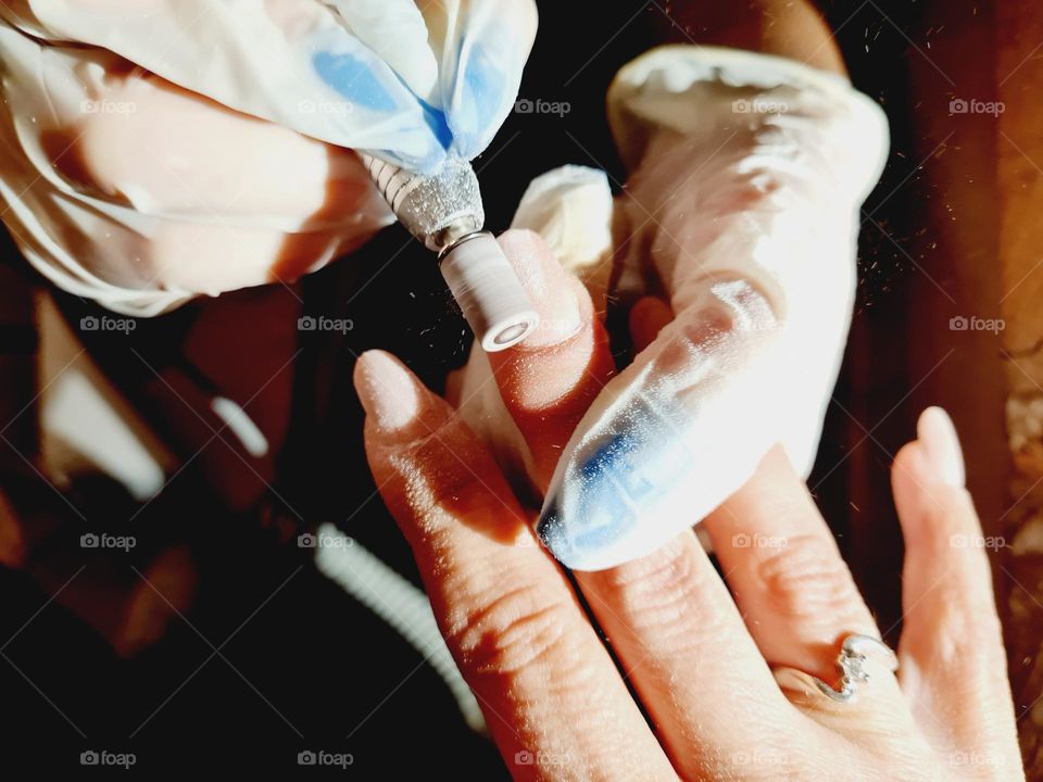 beautician hands detail while performing a nail reconstruction with acrylgel technique