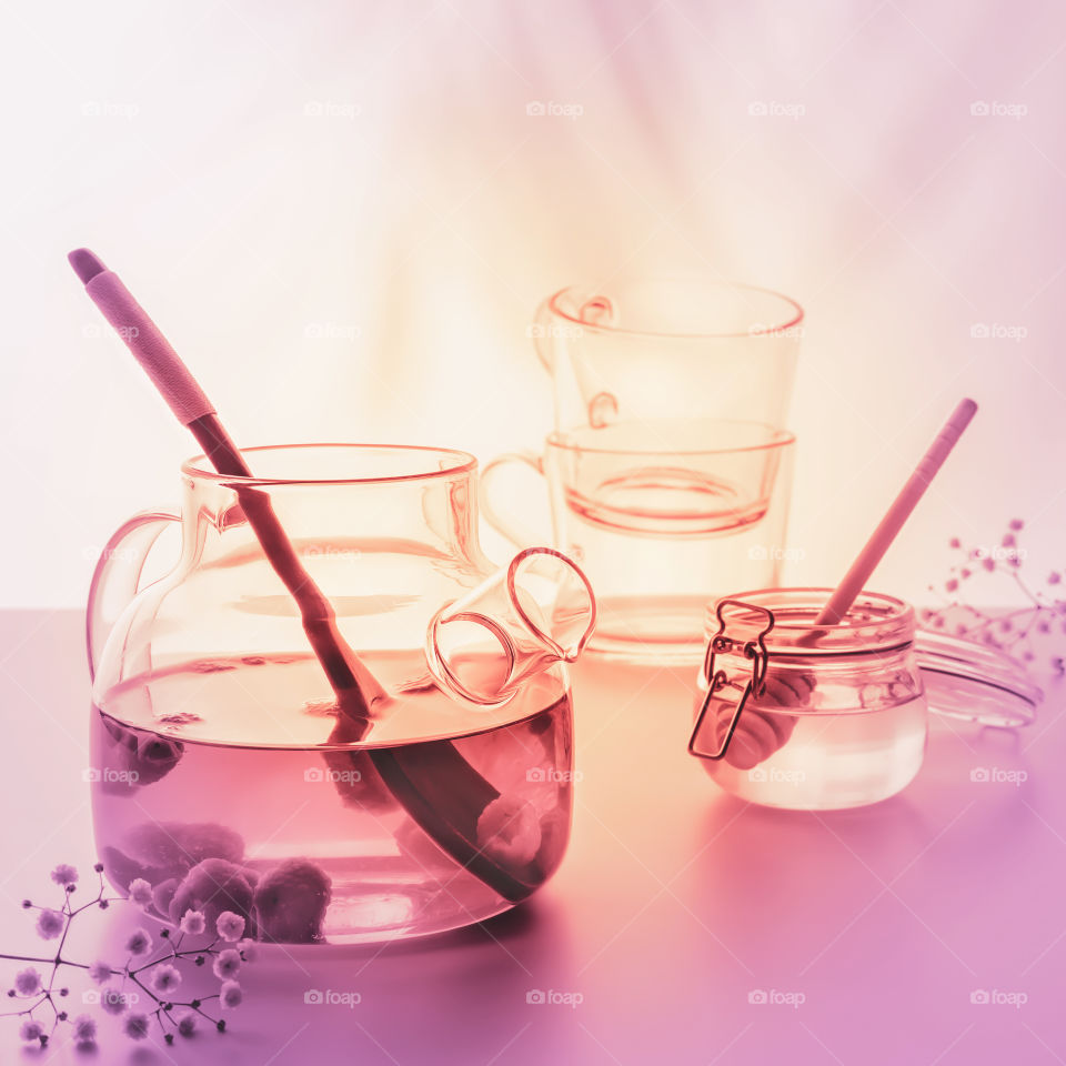 Blurred summer relax tea composition with glass teapot, jar with honey and two glass cups on light sunset background with palm shadows. Healthy no alcohol natural calm drink. Very Peri coloristic