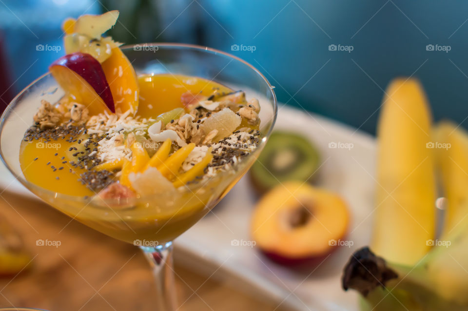 Fun entertaining party smoothie bowl with ginger, peach, coconut, mango, chia seed, oatmeal and black cherry in martini glass on table artisanal food photography
