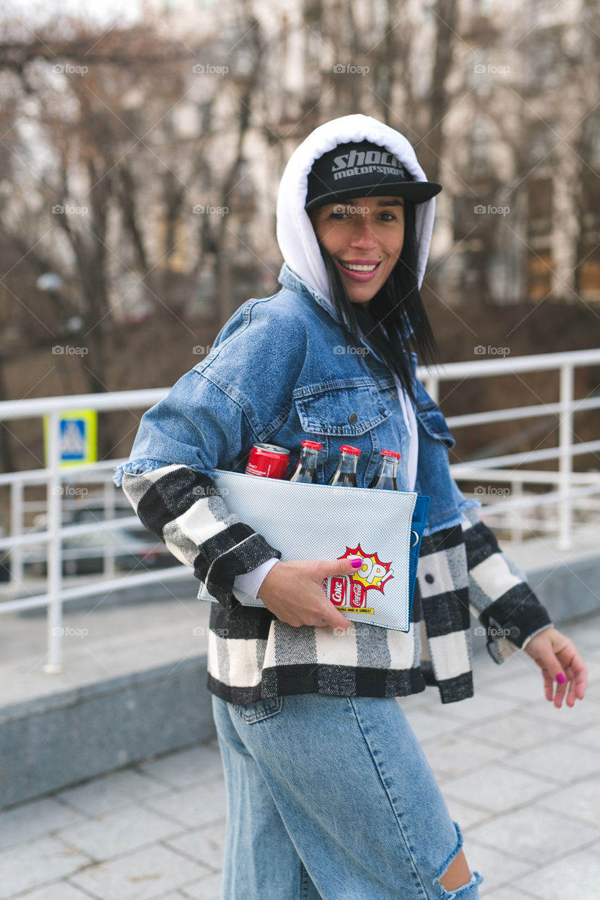 beautiful stylish girl, in denim clothes, walks around the city in her hands with Coca-Cola, spring, emotions, happiness