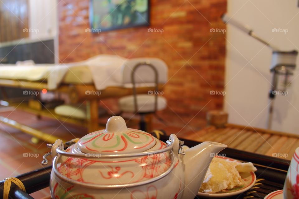 Teapot and cup of tea with candied ginger on a tray and a brown wooden table.