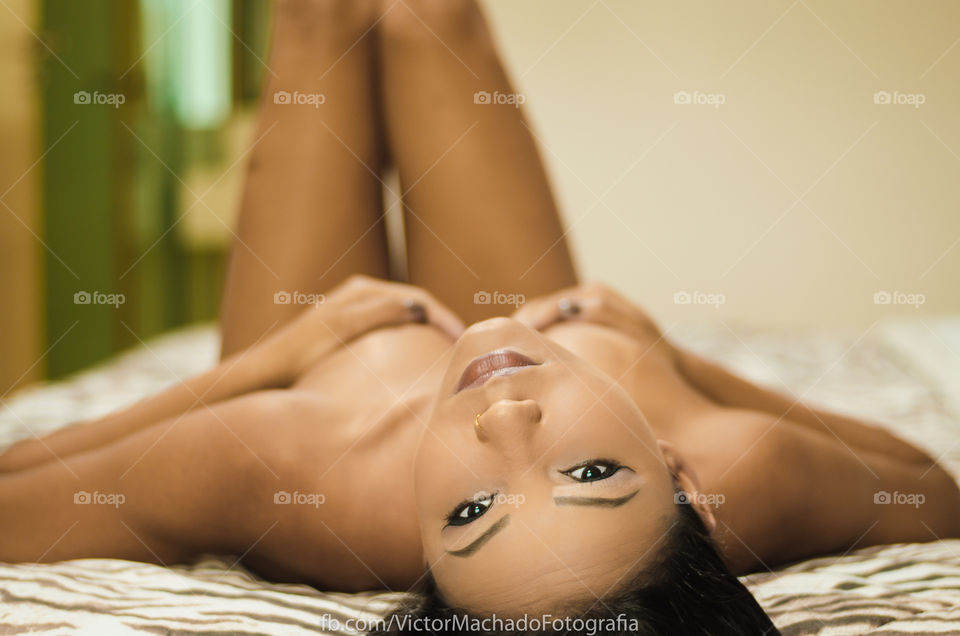 Nude woman covering her breast lying on bed