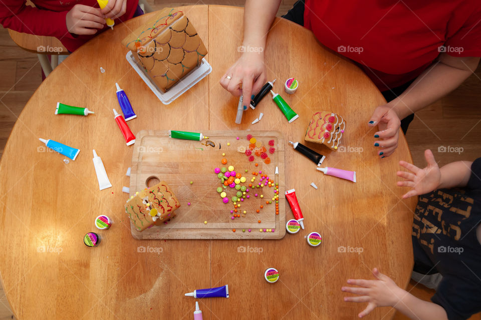 Decorating gingerbread houses with sweets and candies and glitter. Children with mother.