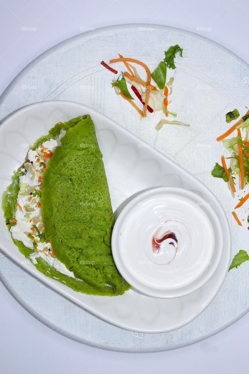 Spinach pancakes filled with cream cheese and vegetables in a white plate on a wooden background.  Top view of food