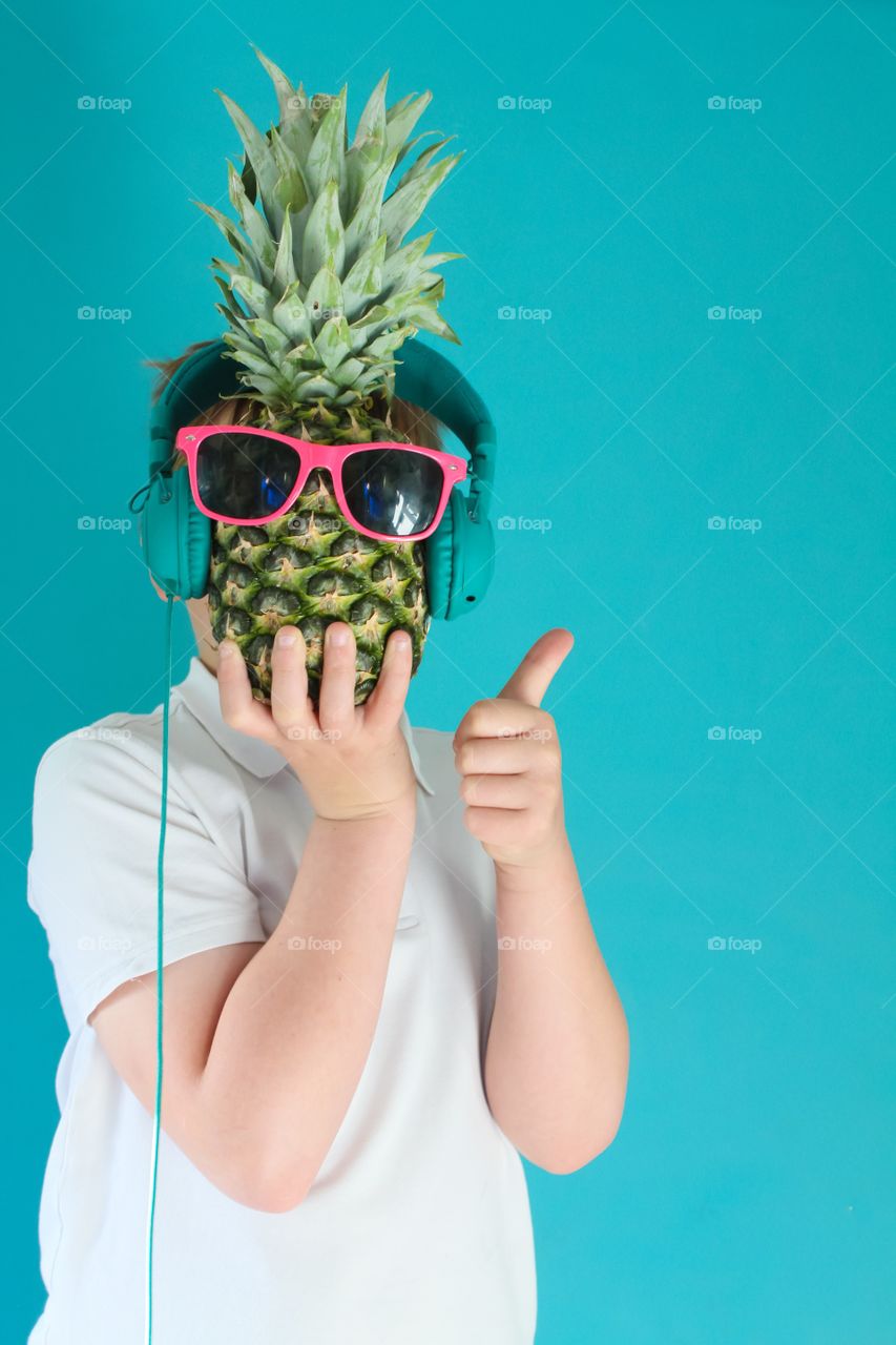 Teen holding a pineapple wearing sunglasses and headphones 
