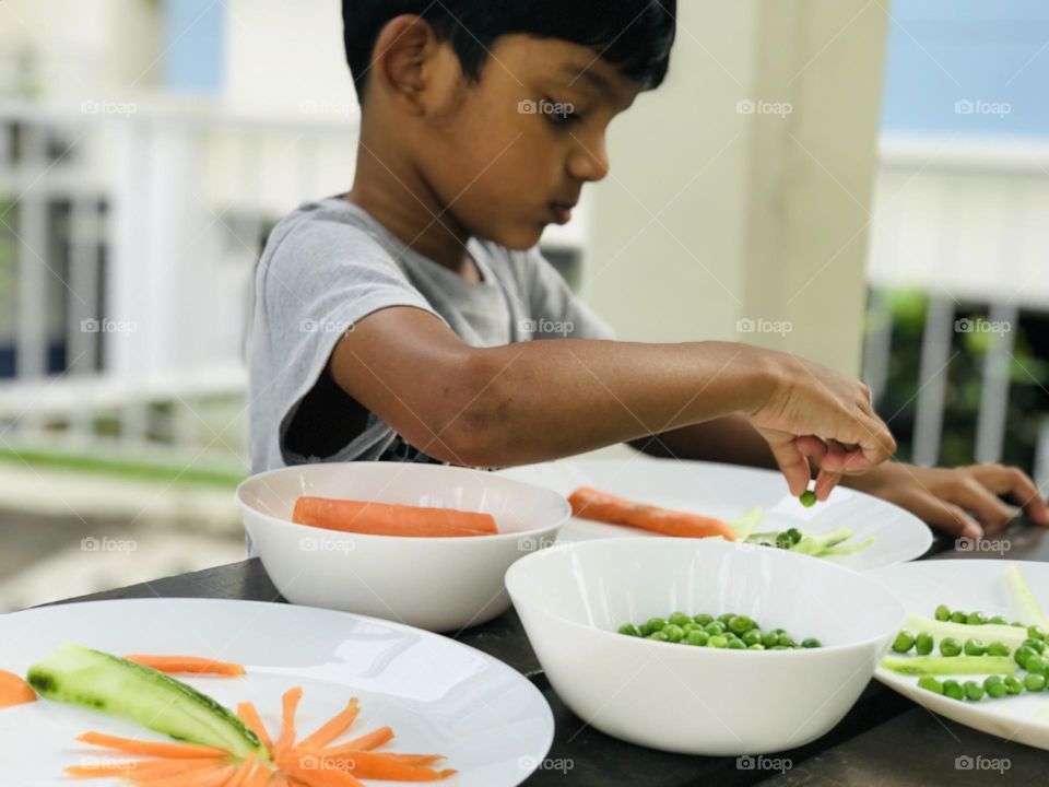 Boy making shapes of sun and palm tree with vegetables like carrots and green peas 