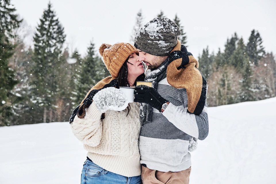 Cheerful young Caucasian couple having a cup of coffee while kissing in the snow