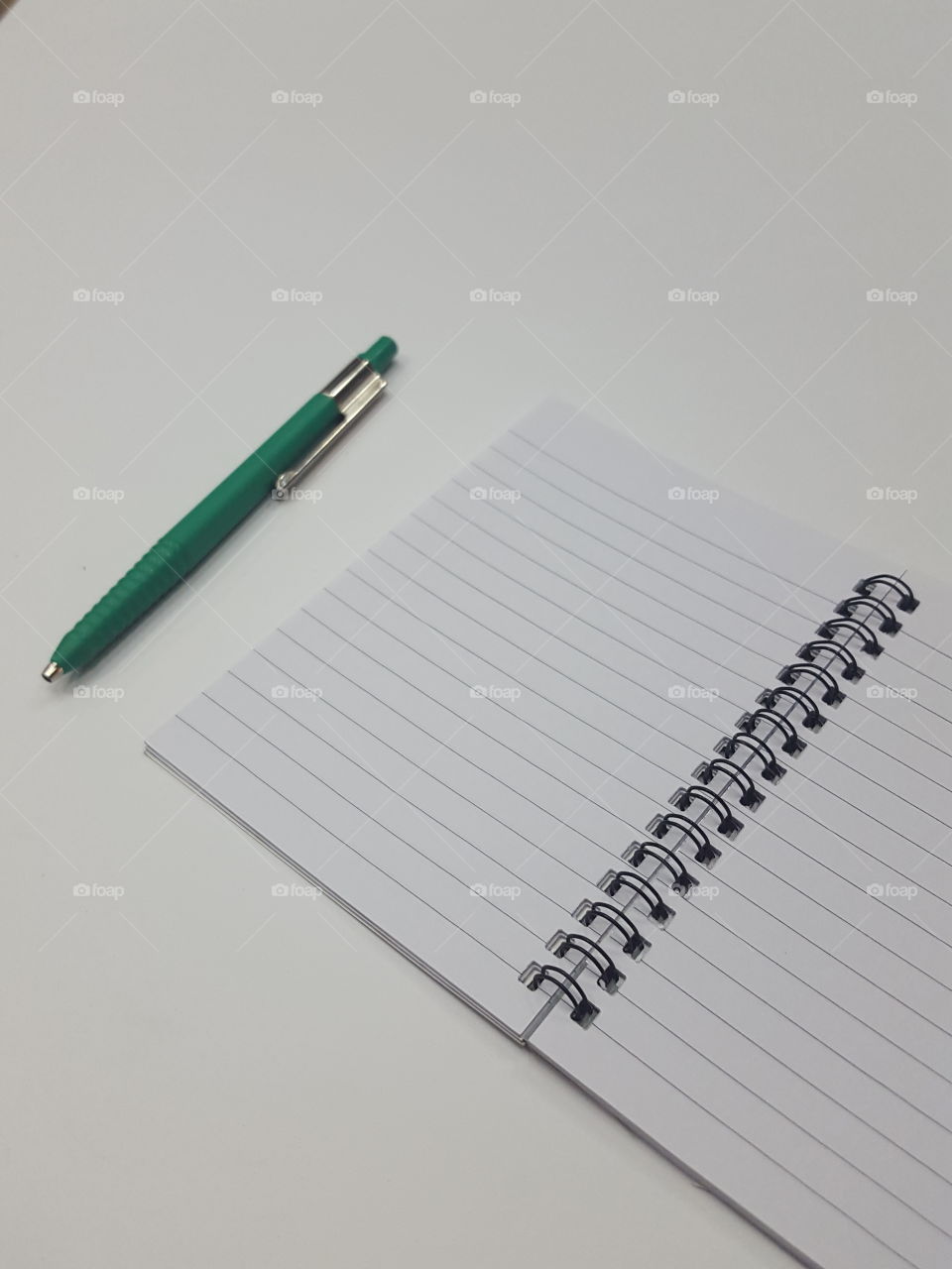 Green plastic ball pen and open ruled spiral notebook