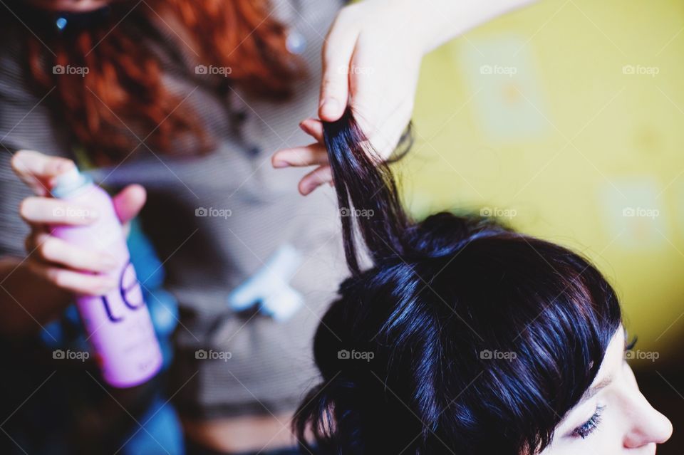 Hairdresser using hairspray on client's hair at salon