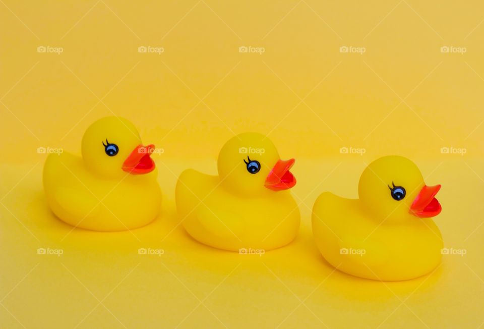 Three yellow rubber ducks in an angled row on yellow background 