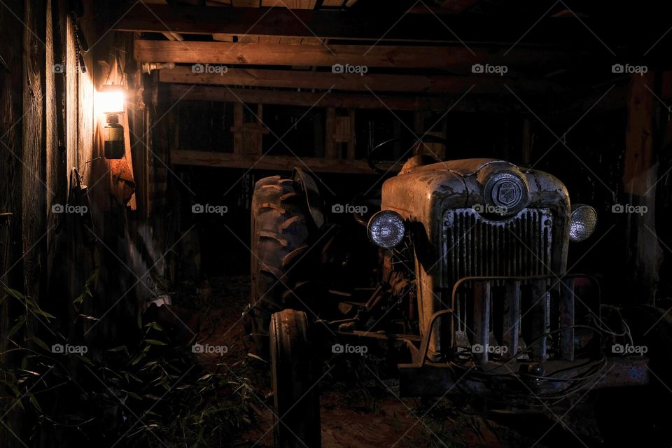 Foap, Day and Night: A rustic nighttime image of an old antique tractor in the bay on the barnside illuminated by the glow of a lantern. 