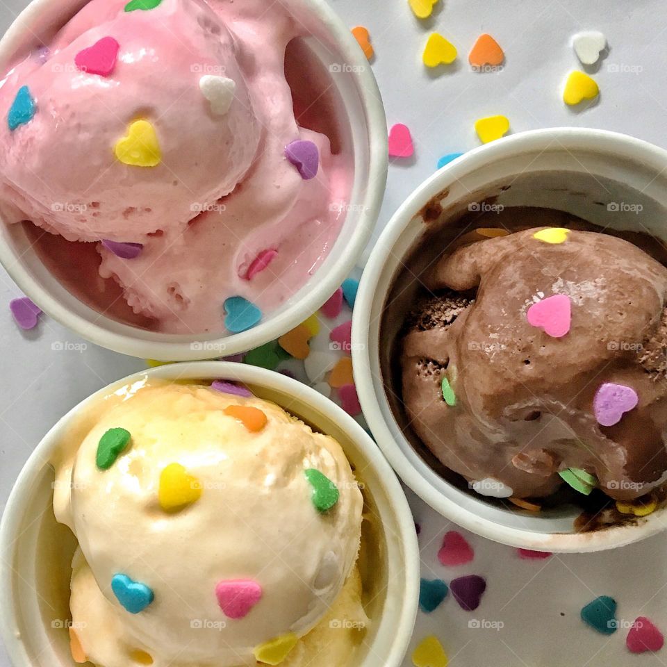 Flat lay food; bright, colourful and delicious ice cream in flavours of vanilla, strawberry and chocolate topped with sugar hearts