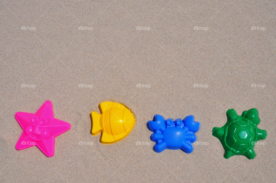 Colorful sand toys lined up on the beach. . Pink Starfish, yellow Fish, blue Crab, green Turtle. 
