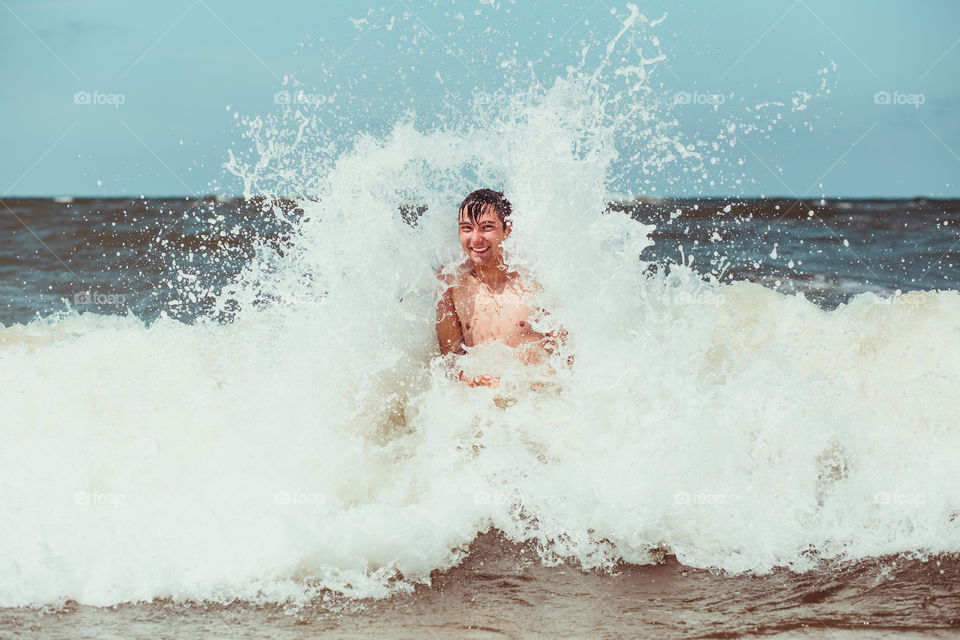 Young man enjoying the high waves in the sea during a summer vacations. Spending a summer holiday by the sea