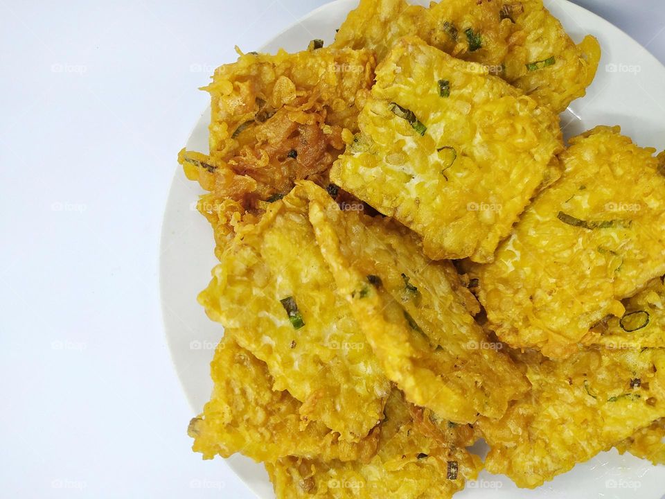 Flour fried tempeh is Indonesian traditional fried food made from tempeh covered in flour batter with a mixture of sliced leeks and spices, isolated on white background