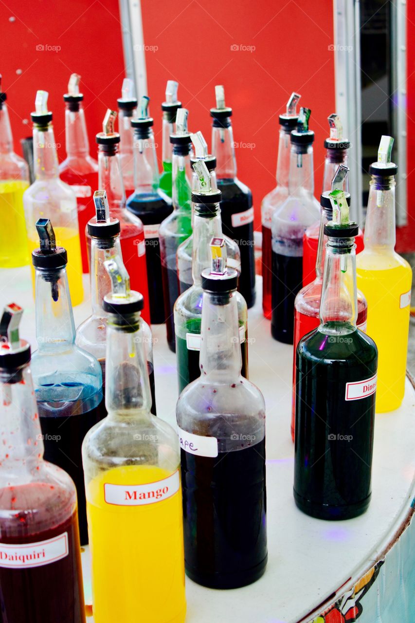 Bottles of assorted, exotic flavorings for sno cones outdoors on a round white table  