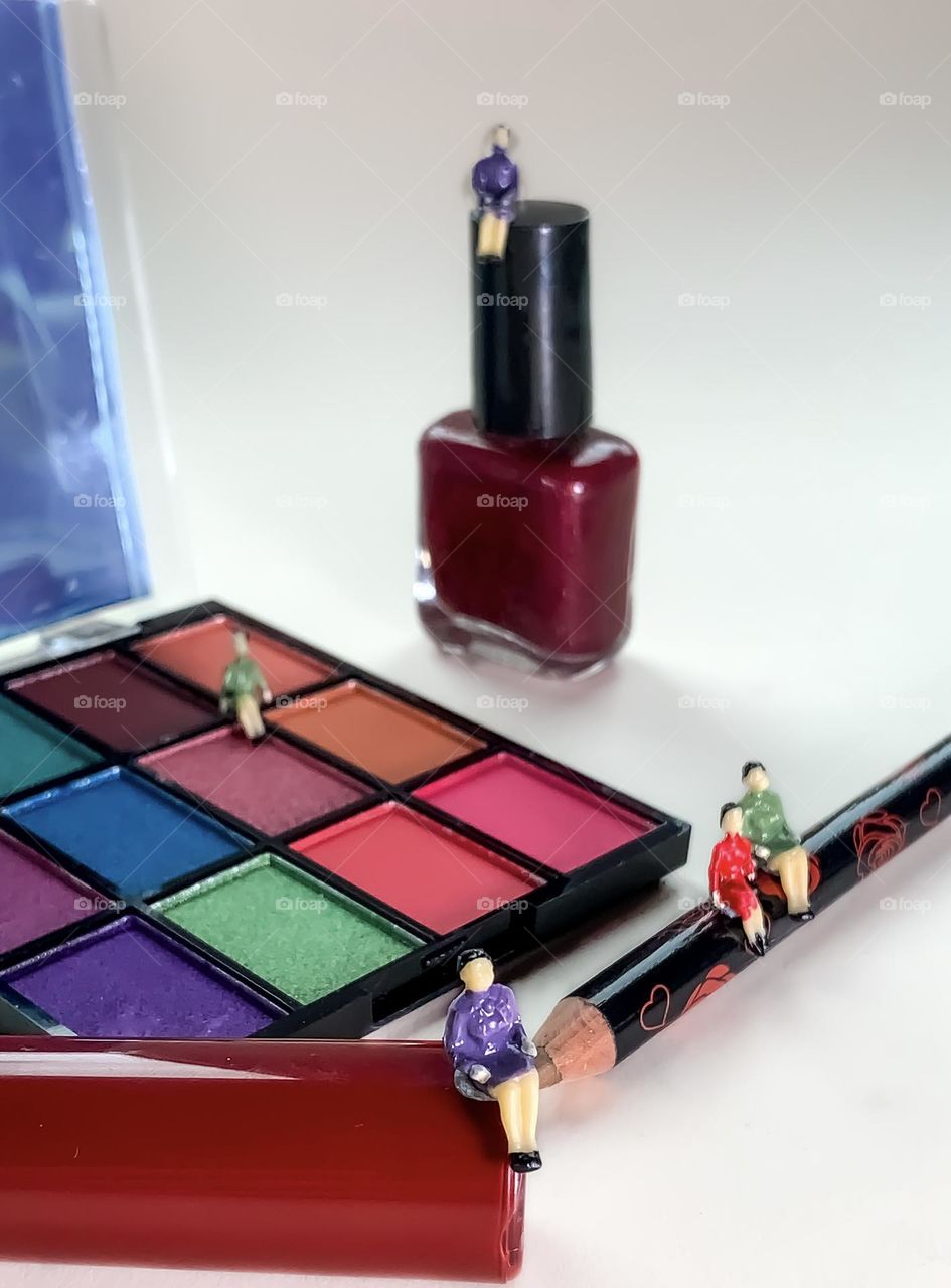 Tiny people seated on assorted colourful cosmetics